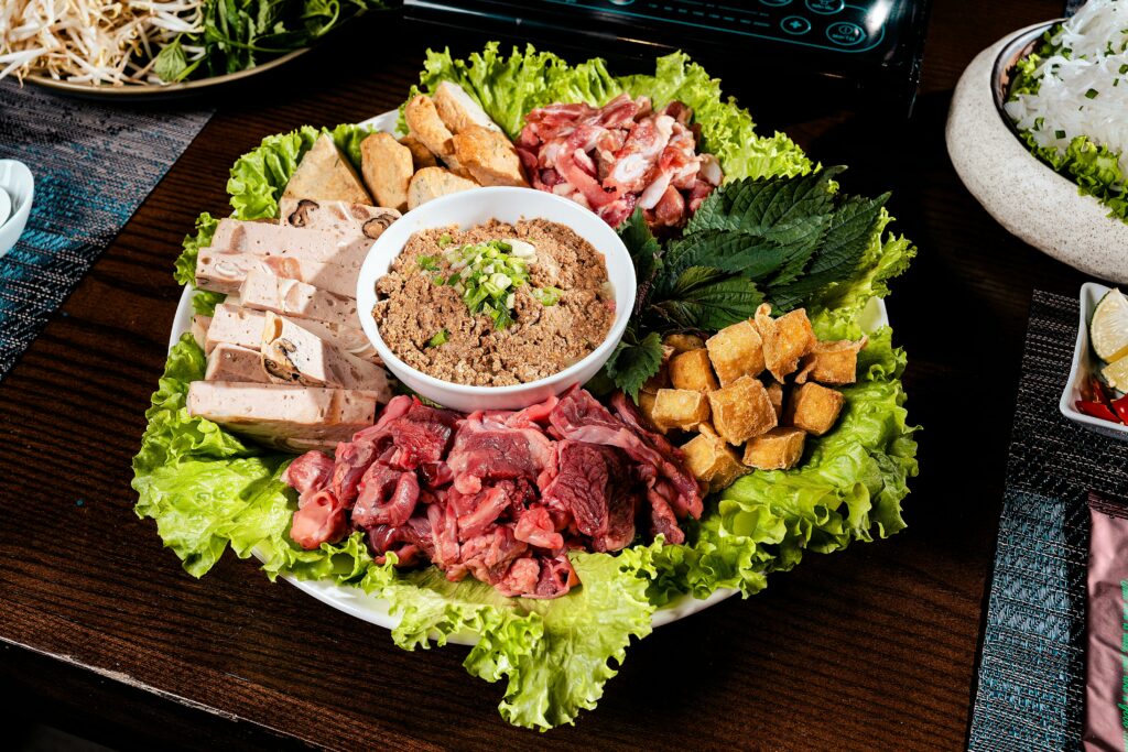 A vibrant display of Vietnamese hot pot ingredients including meats, tofu, and leafy greens on a platter.