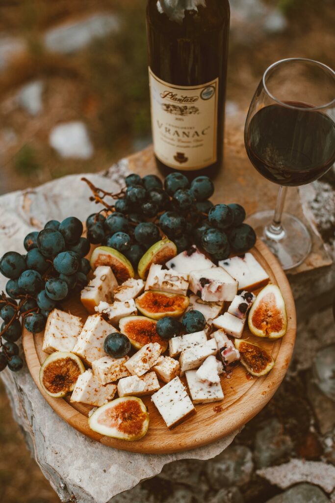 An elegant setting of wine, cheese, and grapes on a wooden platter outdoors.
